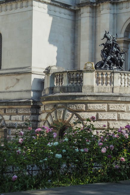 The image shows the exterior of the Tate Britain art gallery with its neoclassical architectural style, featuring tall columns and a large, ornate dome with detailed patterns. In the foreground, part of a van used for house removals is visible, with the vehicle parked close to the gallery entrance on the street. Behind the van, a streetlamp is present, and the sky above is partly cloudy with patches of blue. The scene depicts the process of furniture and packing materials being prepared for home relocation, with visible cardboard boxes and protective wrapping on furniture inside the van, illustrating a loading process typical of professional removals services by Movers Pimlico near the Tate Britain location, supporting efficient furniture transport and logistical coordination for house moves.